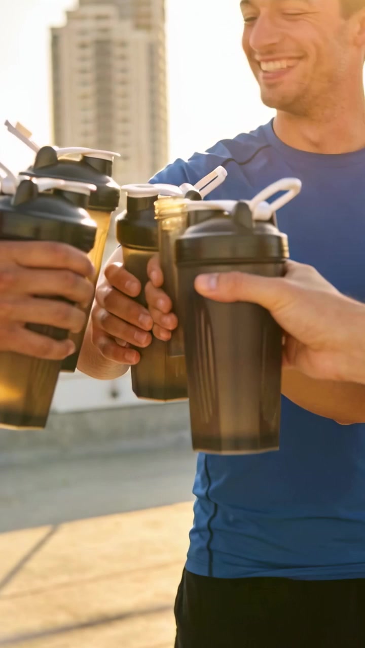 Video verticale: Uomini che brindano dopo l'allenamento sul tetto, con un uomo in maglietta blu che tiene gli shaker.