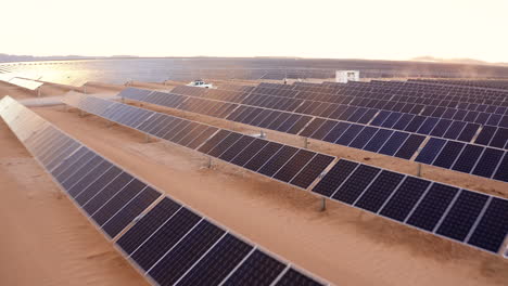 Stunning-aerial-view-of-a-truck-driving-through-thousands-of-solar-panels-with-a-beautiful-sunset-in-the-background