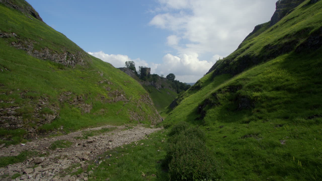Valle panoramica con sentiero roccioso e rovine di un castello in lontananza