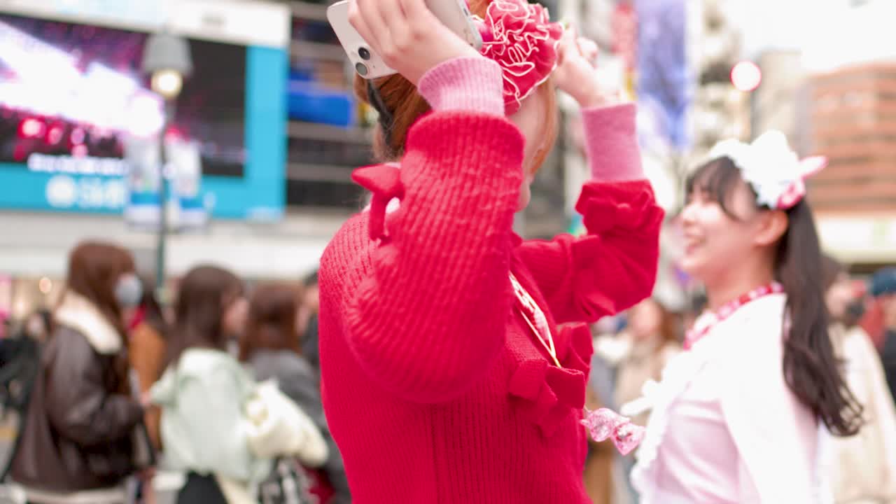 Dos mujeres vistiendo ropa colorida estilo Harajuku ríen y vitorean en el concurrido cruce de Shibuya.