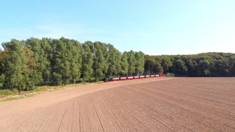 aerial: steam narrow gauge railway in the countryside passing by sown fields and some trees