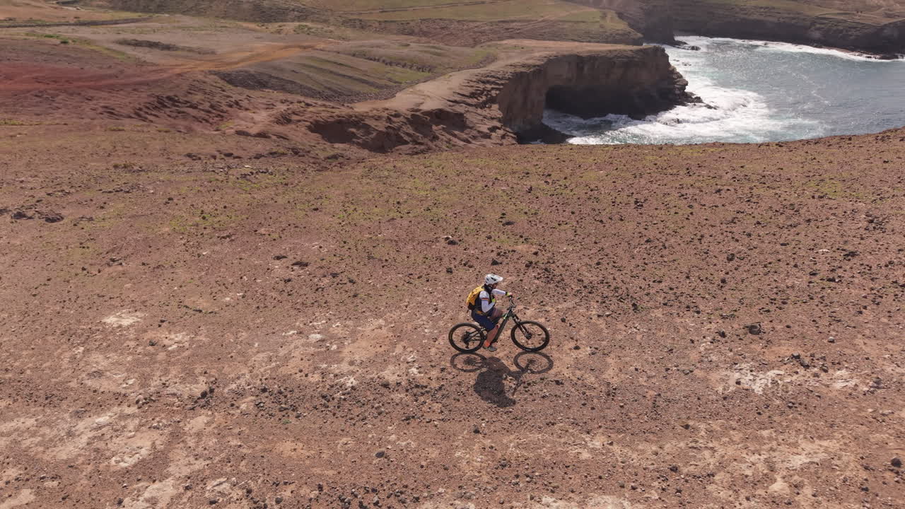 Vista aérea de um ciclista andando de mountain bike em uma trilha desafiadora ao longo de uma costa dramática. Bela paisagem com rochas vulcânicas e ondas do oceano. Costa da Gran Canária.