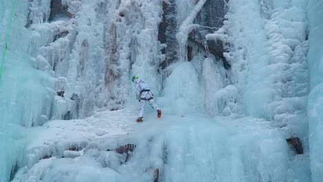 ice climber climbing a frozen icy cliff cascade using two axes - slow motion