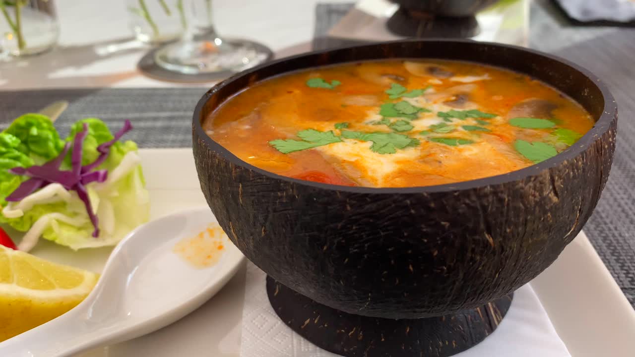 sopa picante tailandesa tom yum con pollo, camarones y verduras en un cuenco de coco, sabroso restaurante de cocina tailandesa, tiro de 4k