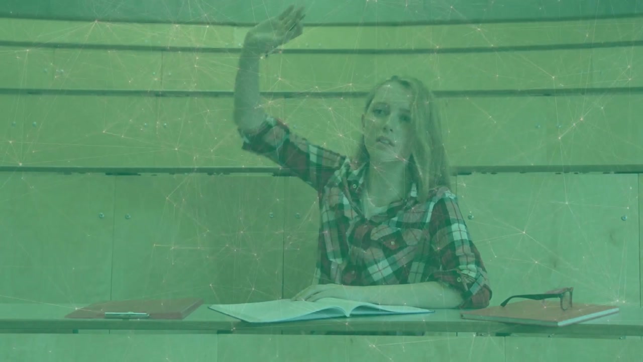 teenage student finishing notes in notebook during lecture then raising hand and resuming writing