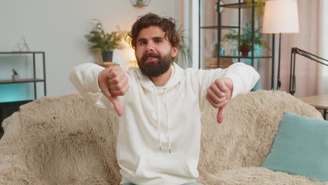 upset unhappy young indian man showing thumbs down sign gesture expressing discontent at home