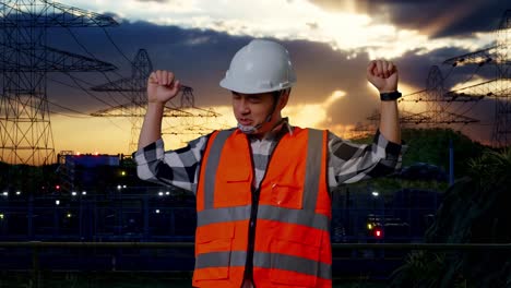 ingeniero asiático con casco de seguridad gritando gol y bailando celebrando cerca de la torre de alto voltaje