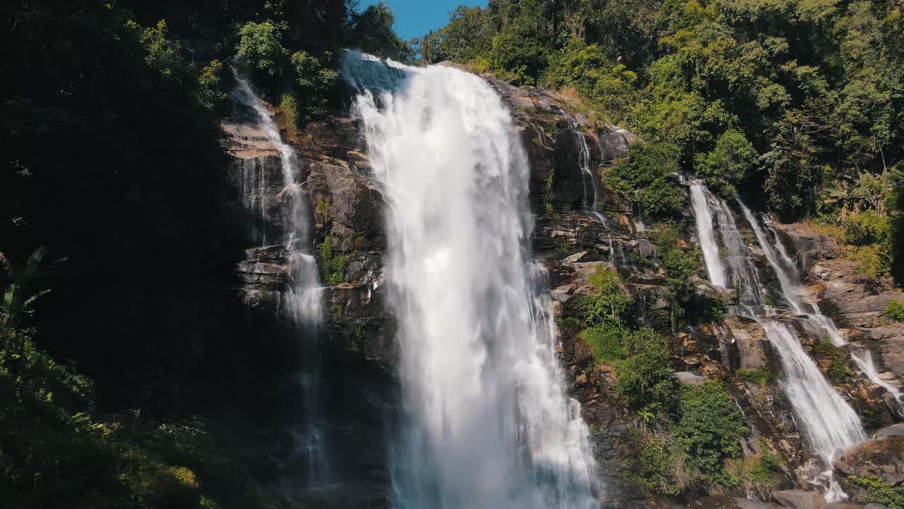 gran cantidad de agua cae sobre la gran cascada de wachirathan entre los árboles verdes y la vegetación en un día soleado
