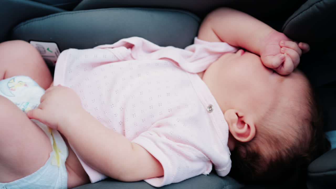 Close up of a baby wearing a pink outfit, peacefully sleeping with a hand near the face