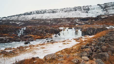 Pan-shot-of-a-waterfall-in-Iceland-surrounded-by-snowed-mountains,-Dynjandi,-Dynjandifoss,-Westfjords