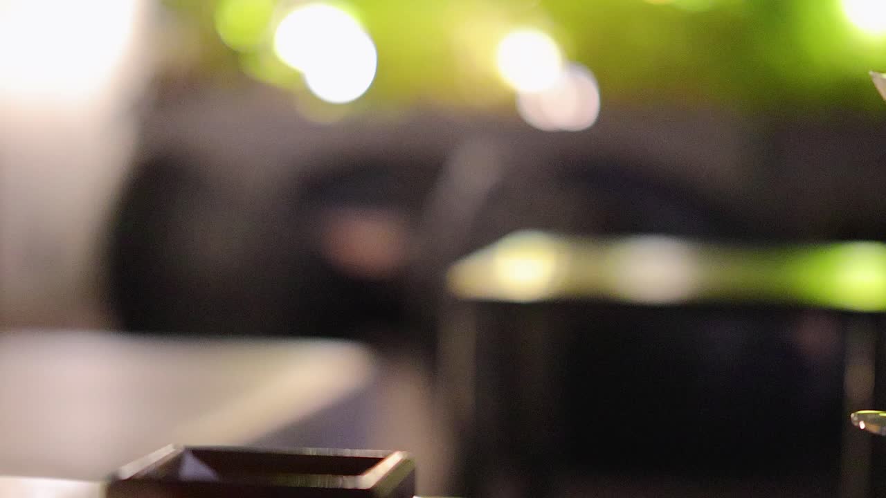 A hand gracefully lifts an espresso martini from a table in softly lit lounge environment