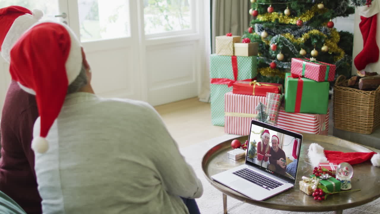 diversas amigas mayores que usan una computadora portátil para una videollamada de navidad con una pareja sonriente en la pantalla