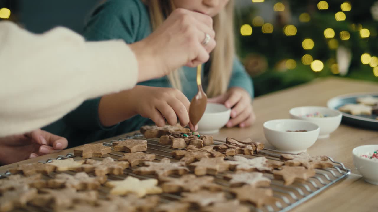 madre y hija caucásicas decorando galletas de pan de jengibre con chocolate y salpicaduras.