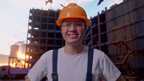 hombre asiático trabajador brazos akimbo mirando a la cámara y sonriendo en el sitio de construcción