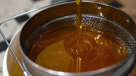 organic fresh honey pouring on the metal sieve. filtering honey right after extraction. close up.