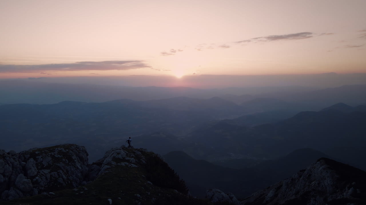 Una ripresa con drone della cima del monte Peca all'alba, con un escursionista in piedi sul crinale della montagna.