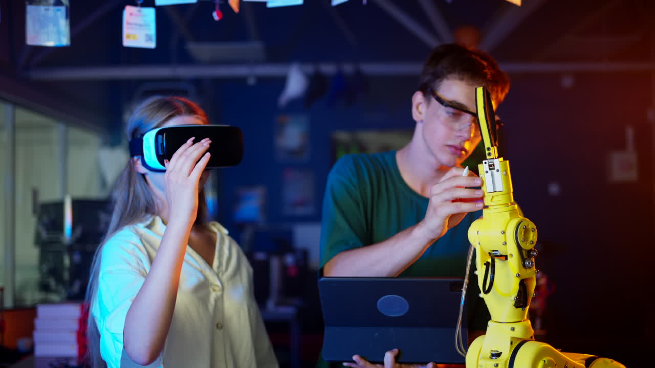 Young engineers with VR virtual reality headset controlling an yellow robotic arm in research laboratory