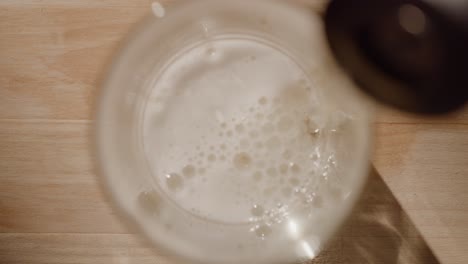 overhead view of alcoholic beverage being poured from a can into a glass cup on a wood surface