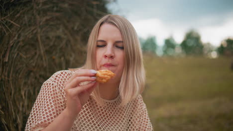 young lady in net top savoring her crunchy pastry while seated in an open field, the peaceful outdoor moment captures a serene atmosphere with nature in the background