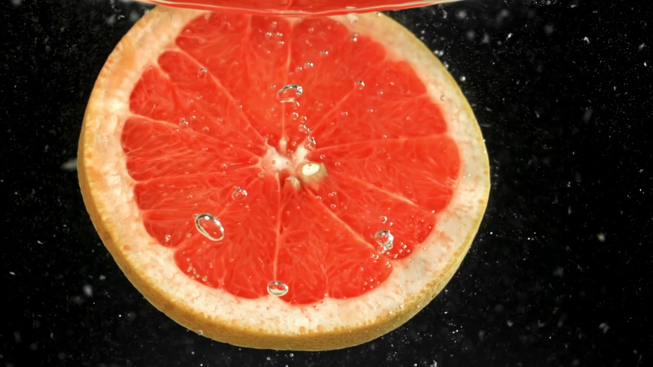 Fetta di pompelmo vivace che affonda in acqua limpida con bolle.