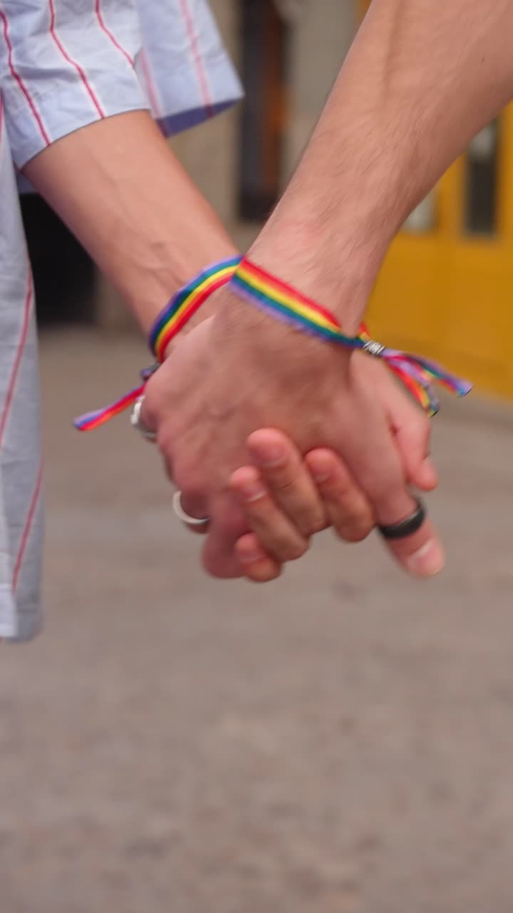 Primer plano de una pareja tomados de la mano con pulseras del Orgullo Arcoíris.