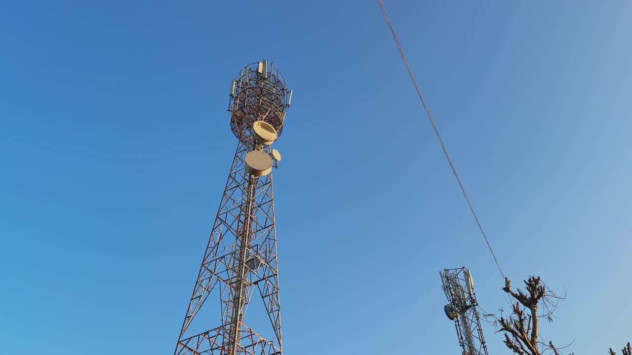 Wide angle view of two telecommunication towers standing under a clear blue sky, showcasing wireless antennas and microwave dishes symbolizing modern connectivity and network expansion