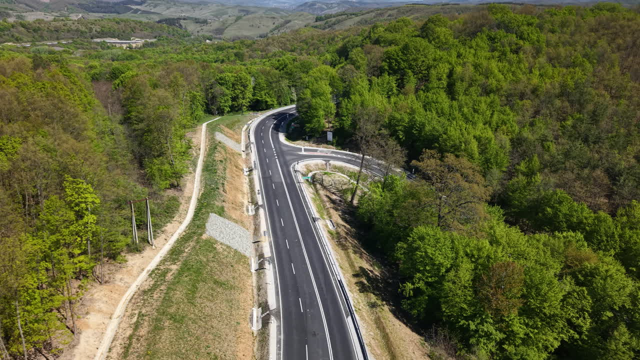 Perspektywa z drona pokazuje krętą asfaltową autostradę przecinającą bujny zielony las w regionie górskim.