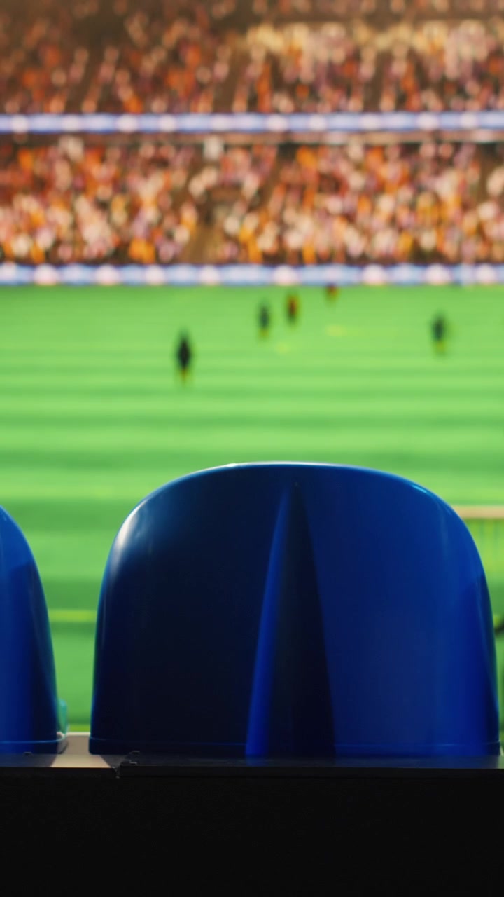 Video verticale. Primo piano dei sedili dello stadio che si affacciano su un campo da calcio sfocato con i giocatori.