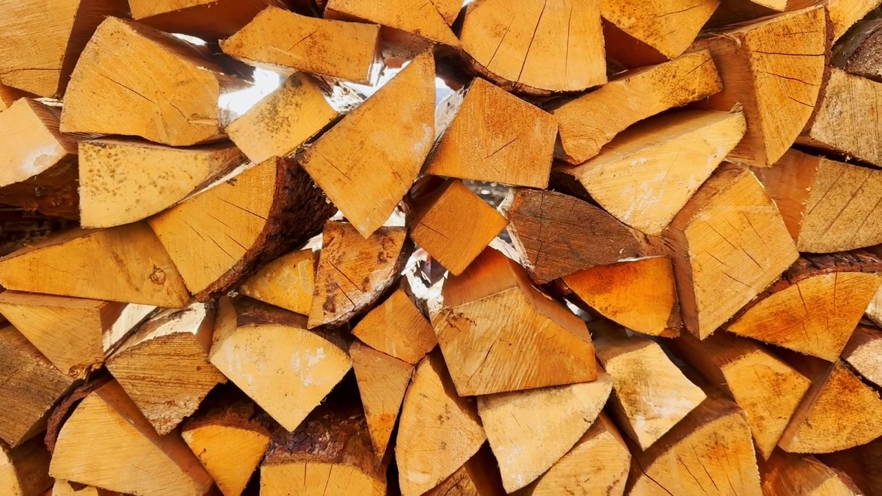 Top-down view of neatly stacked split firewood, showing golden cut log ends, bark edges, wood grain, and a rustic heating supply pattern.