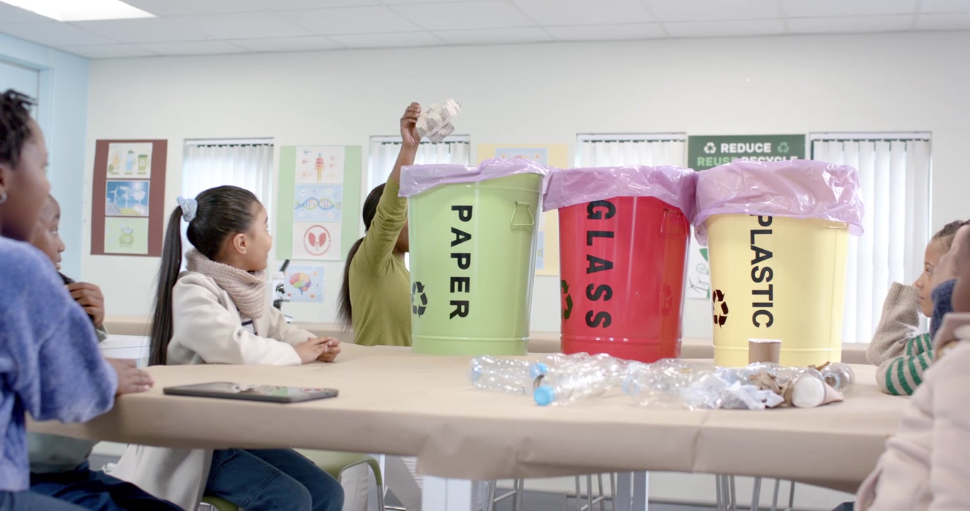 学校で手を挙げる子供たち、先生が卵のカートンを取り、紙を緑のゴミ箱に分別する様子を見せる