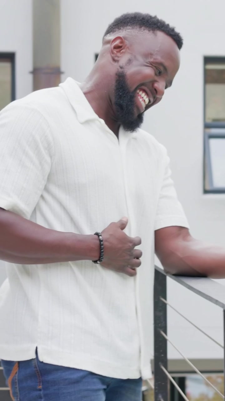 Vertical video: Smiling at pink phone, man leaning on metal railing, reading replies in white shirt