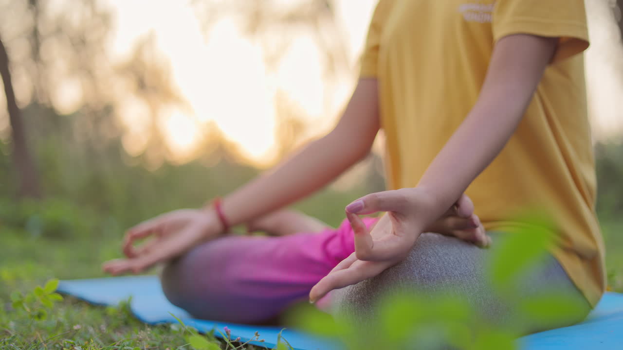 Close up shot of a woman sitting in lotus position on a yoga mat at outdoor during golden hour