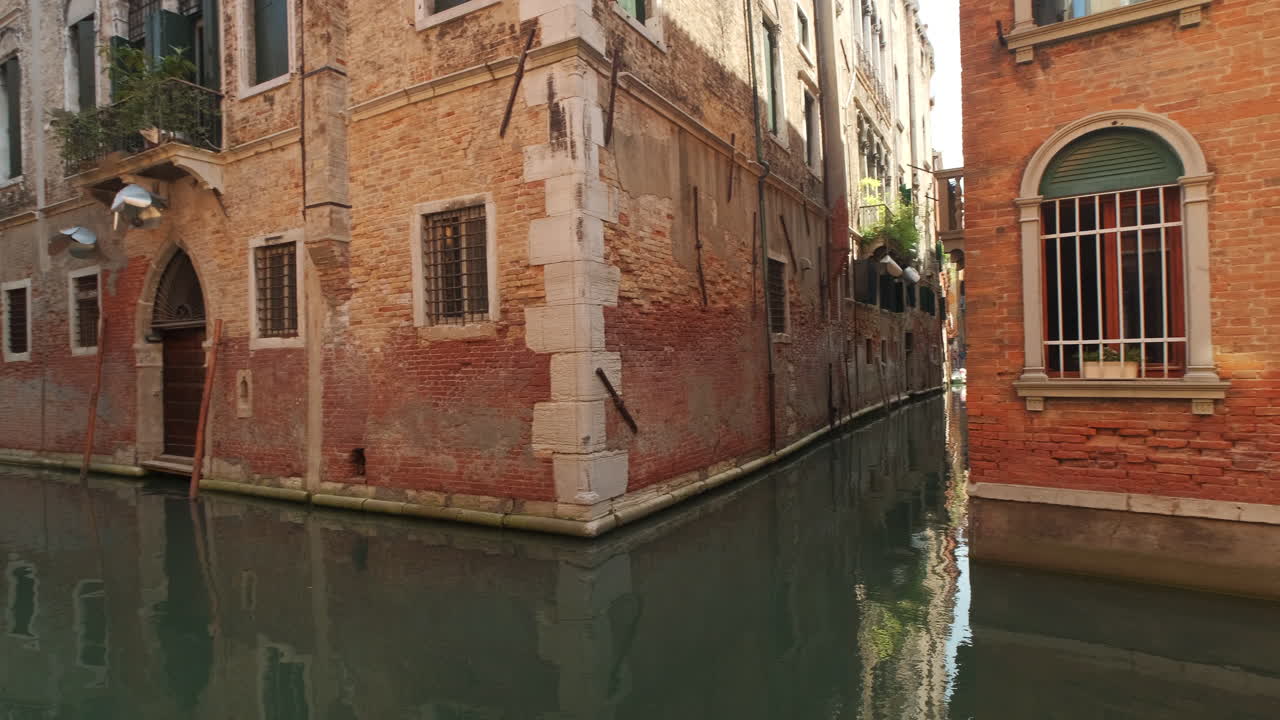 Pov Dolly shot between narrow gate and beautiful pan of italian canals with surrounding old buildings in summer. Venice,Italy
