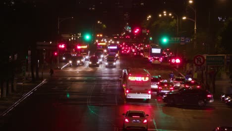 busy street traffic at night in taipei with cars and buses with headlights on while traffic lights turn red to green – wide shot