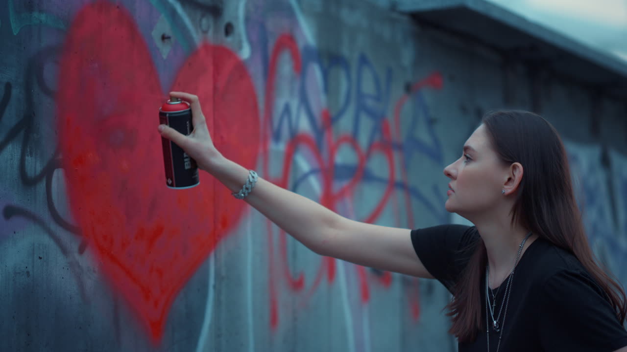 chica dibujando graffiti en la pared. mujer enfocada pintando corazón con botella de aerosol