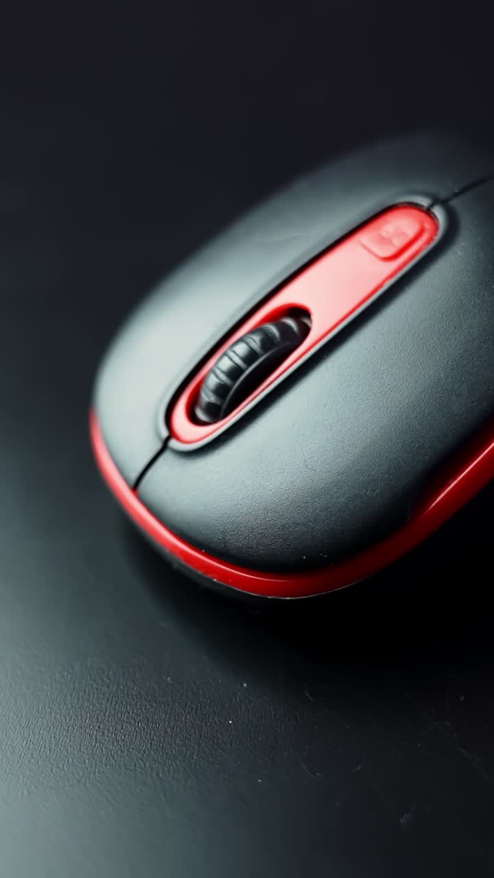 Vertical macro of a black-and-red computer mouse with scroll wheel on a dark desk, moody low-key lighting and copy space for tech or office concepts