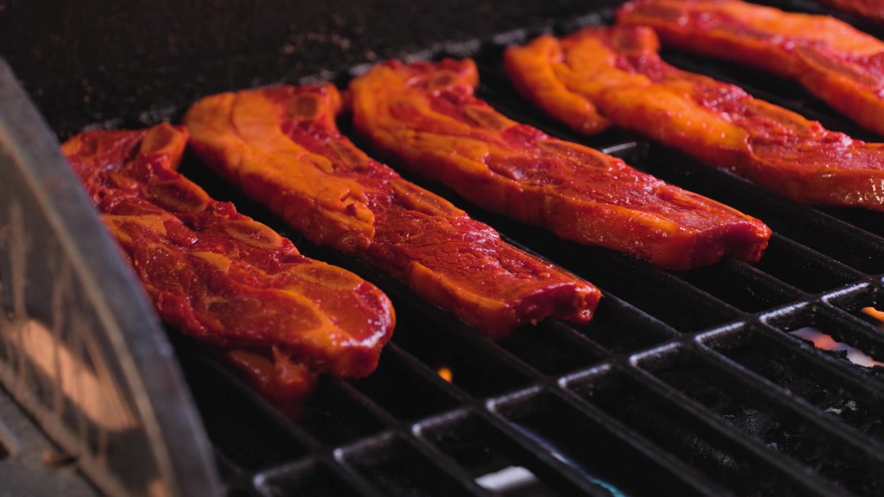 Riprese ravvicinate di barbecue che mostrano una panoramica a sinistra per inquadrare tutte le costine di manzo sulla griglia durante la preparazione delle costine di manzo su una griglia calda.