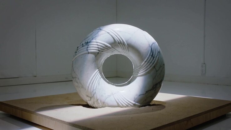 Skiftende lys, der stryger hen over marmor-torus-skulptur på træplatform i studie, og afslører riller