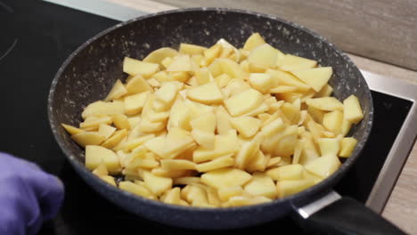 Two-hands-with-gloves-puts-raw-potatoes-in-skillet-on-stove,-close-up