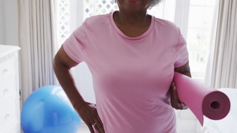 retrato de una mujer afroamericana mayor con un tapete de yoga sonriendo en casa