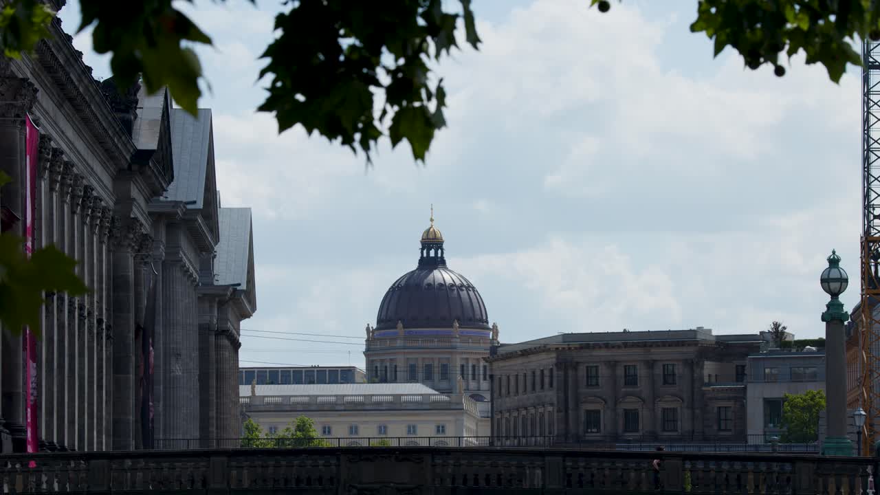 Camera slowly pans across historic dome and classical columns under leafy trees, daylight, urban setting