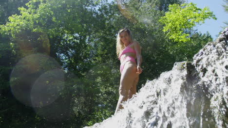 Confident-young-woman-poses-on-the-edge-of-a-waterfall-in-the-forest