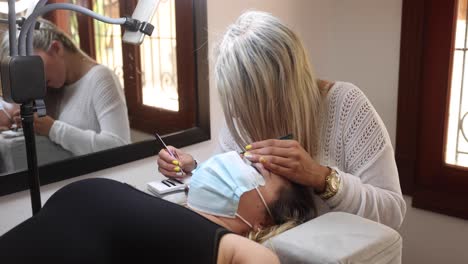 Beautician-applying-eyelashes-on-face-of-woman