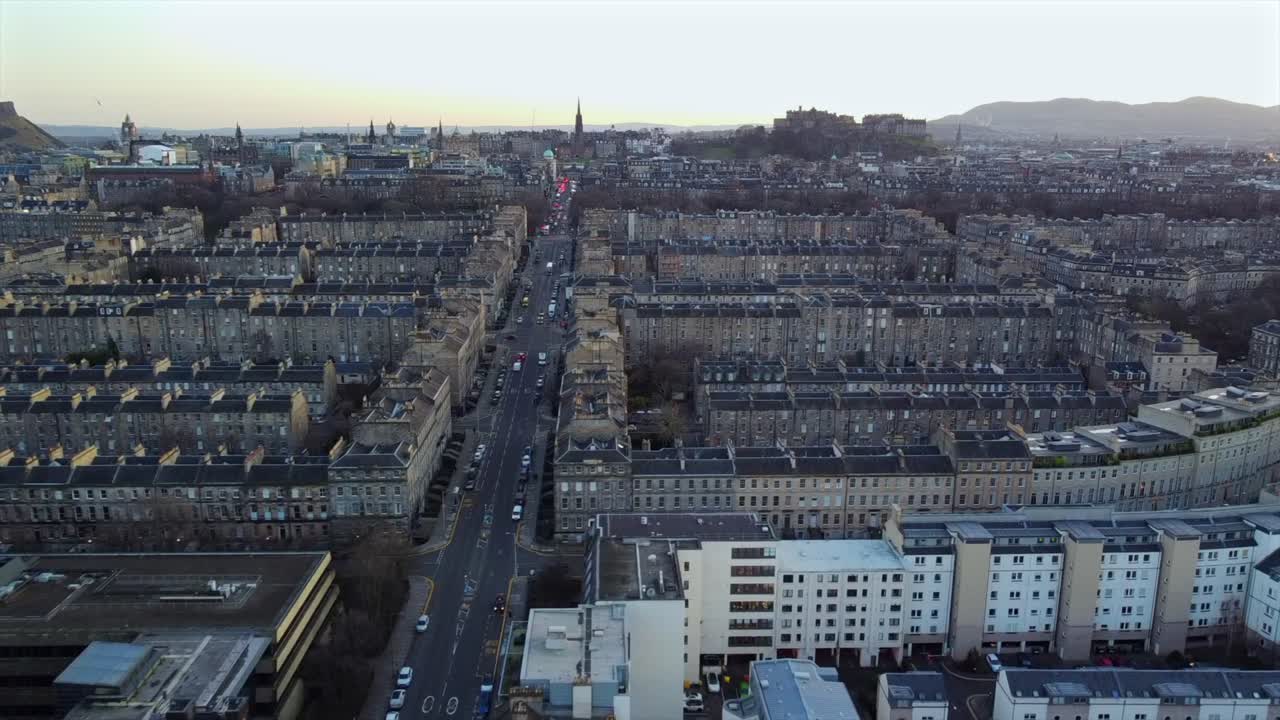 Expansive view of Edinburgh’s iconic city layout, showcasing symmetrical streets lined with historic buildings. The shot leads towards Edinburgh Castle, with Arthur’s Seat visible in the distance.