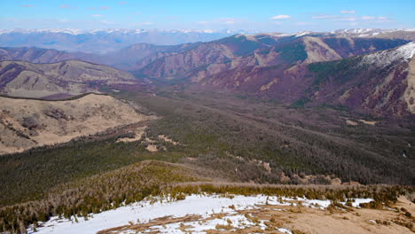 vast mountain landscape with forests and snow patches
