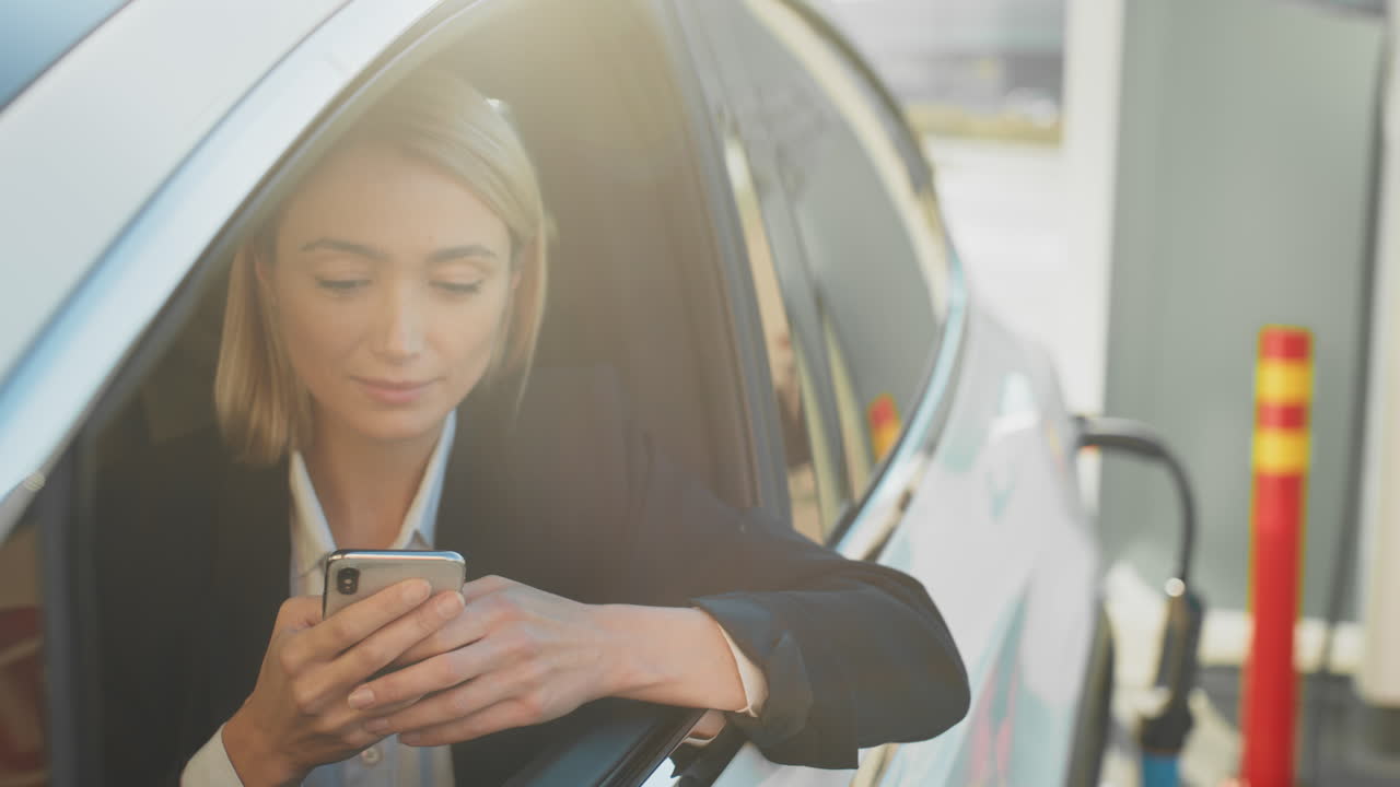 mujer usando un teléfono inteligente en un coche eléctrico en una estación de carga