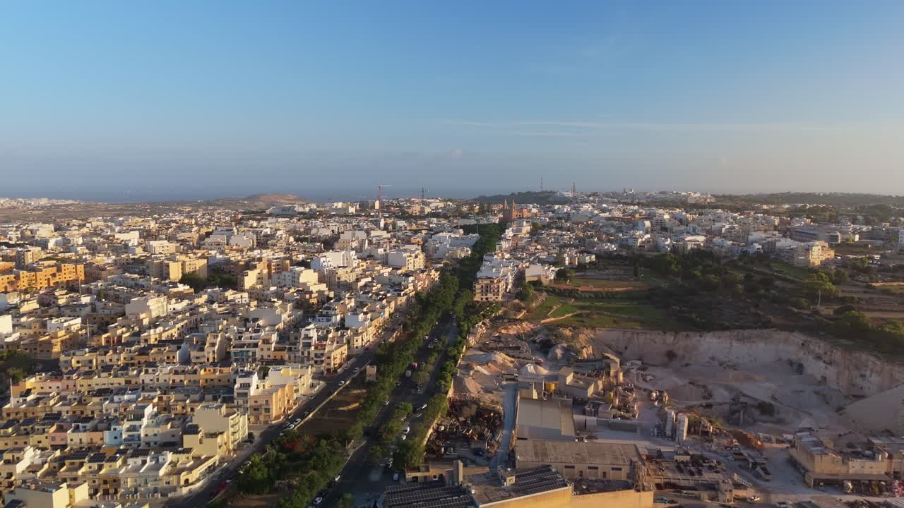 Drone orbital shot around Naxxar, Malta, revealing the city’s dense architecture, quarry, and surrounding countryside under warm morning light