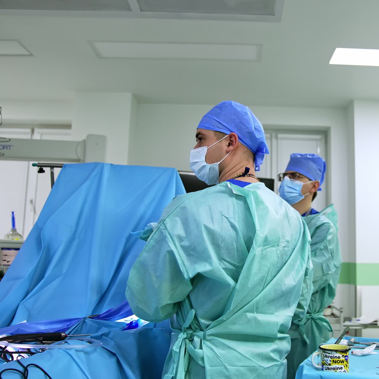 Chief doctor and his assistant look intently on the screen during surgery. Make nurse standing near the table with instruments