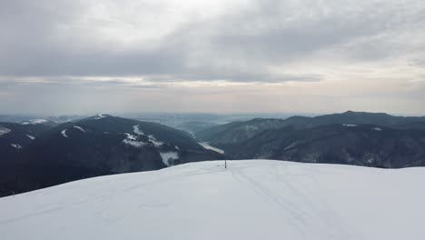 Figura-Solitaria-En-El-Pico-Gainatu-Con-La-Presa-Rausor-En-El-Fondo,-Montañas-Iezer-Papusa,-Arges,-Rumania,-Escena-De-Invierno