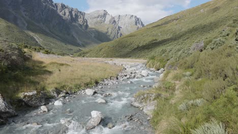 Blue-river-running-down-down-a-valley-in-between-mountains-on-a-sunny-summer-day-in-Rees-Dart-track,-New-Zealand